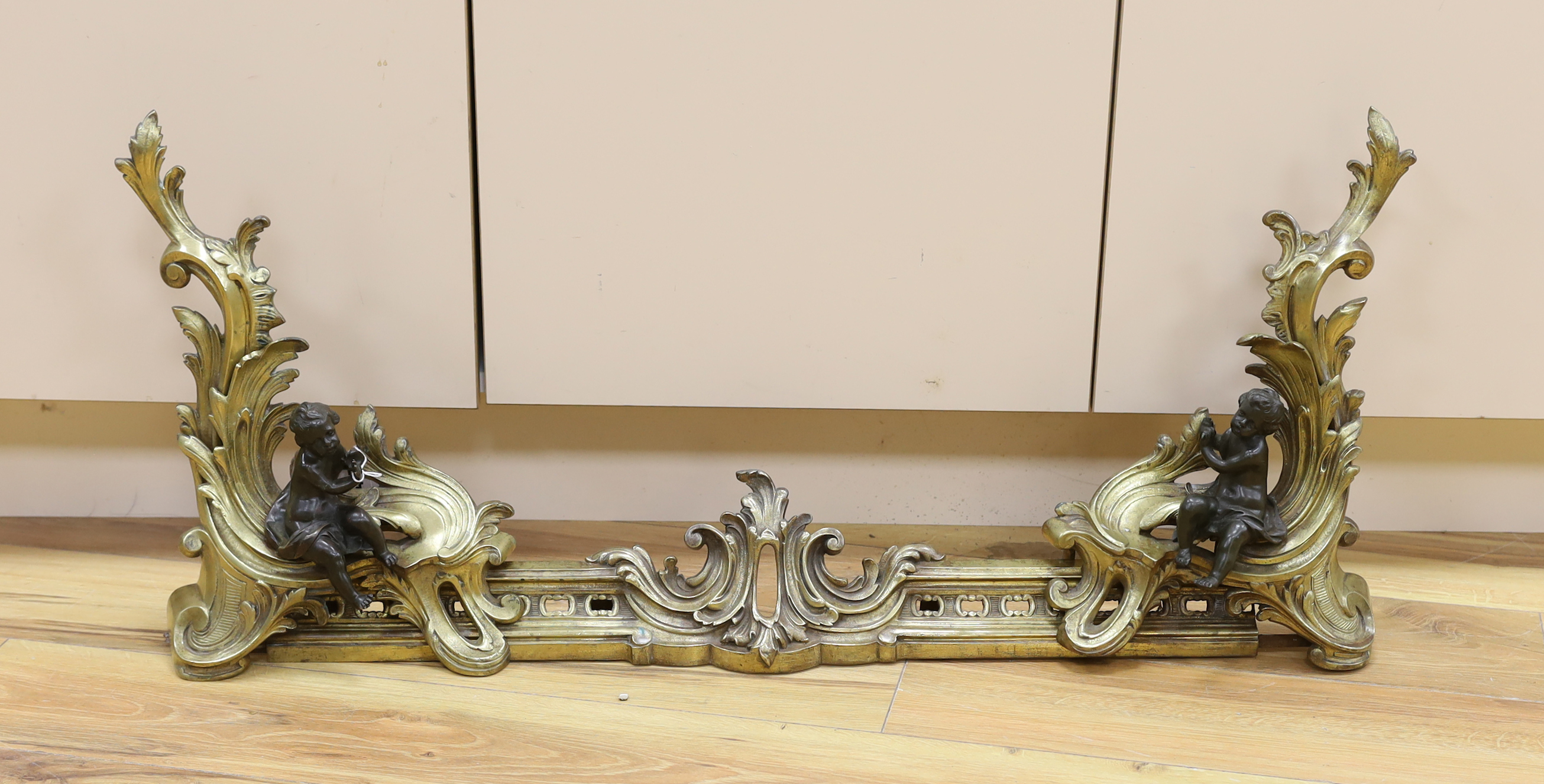 A pair of brass chenet mounted with patinated bronze figures of putti, 97cm wide